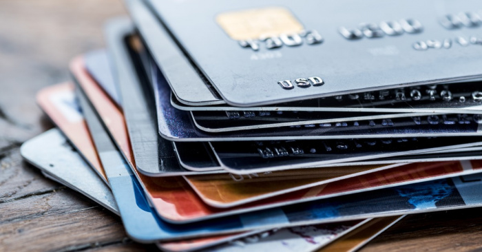 A close-up of a stack of credit cards that are different colors. The credit cards are on a wooden surface.