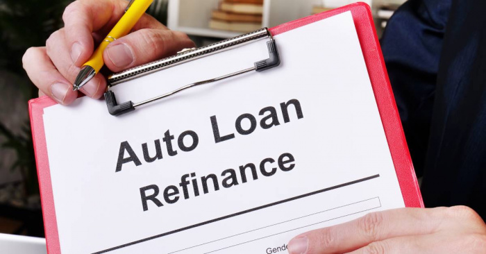 A close-up of a person holding a clipboard with a form titled 'Auto Loan Refinance.' The person is also holding a yellow pen.